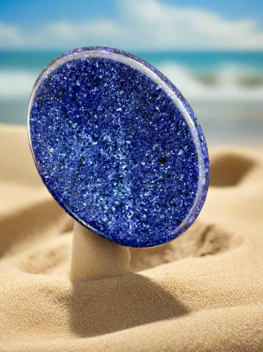 Oval blue stone on sand with a beach background.