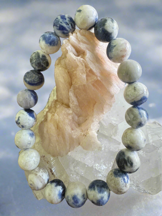 A beaded bracelet of white and blue speckled stones encircling a pale pink and white crystal formation.