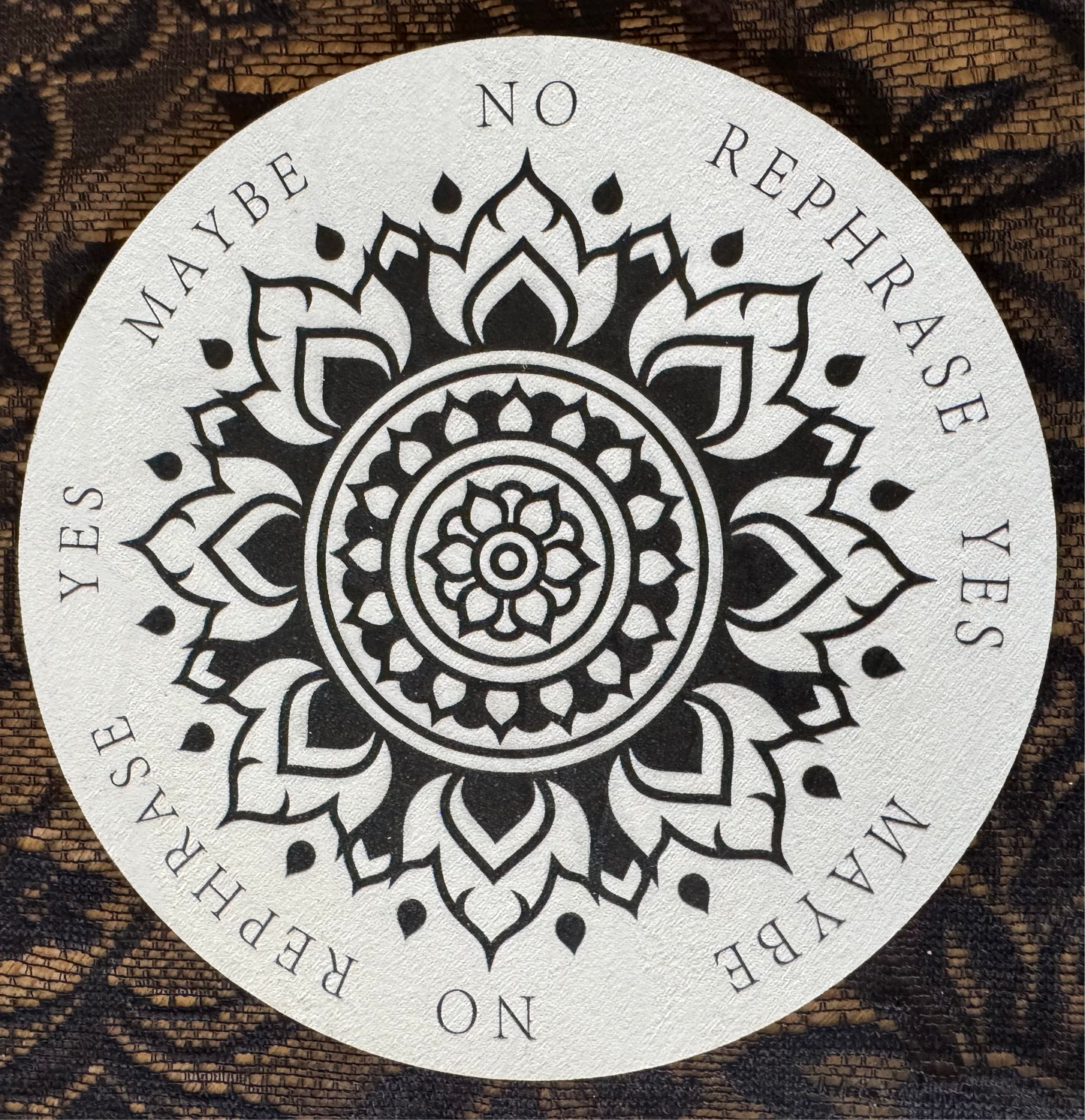 Circular divination board with floral mandala design. "Yes," "No," "Maybe," and "Rephrase" options. Lace background.