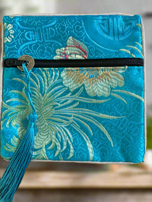 Close-up of a blue floral brocade pouch with a black zipper and a blue tassel with a Chinese coin.