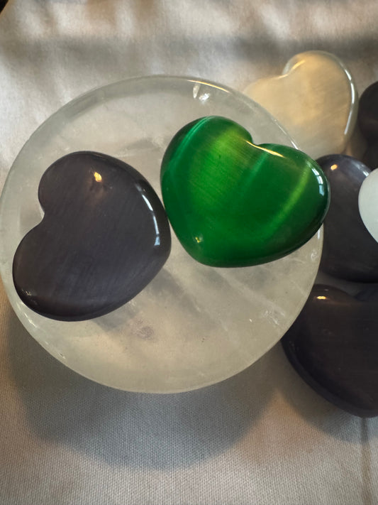 Several heart-shaped gemstone cabochons on a milky white dish, arranged on a textured white surface.