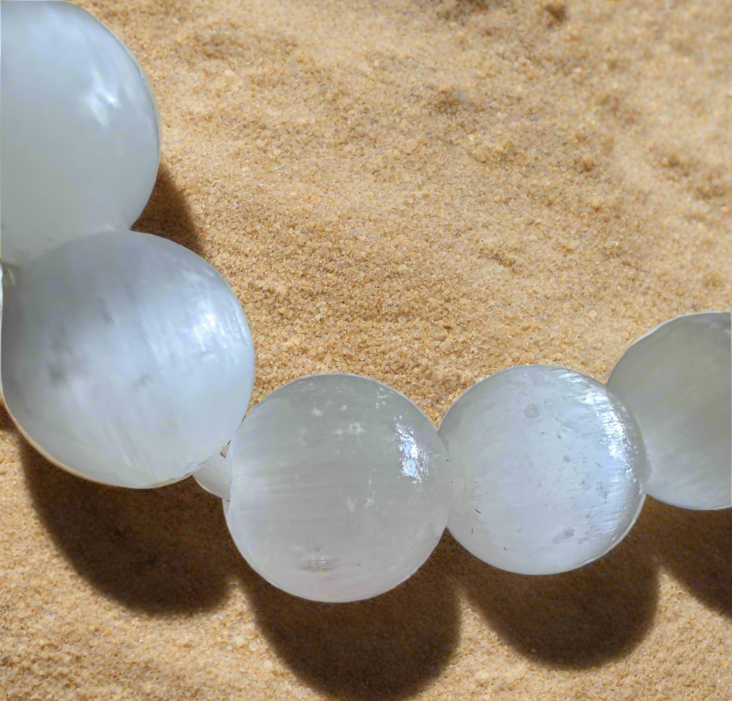 Close-up of a selenite bead bracelet on sand.