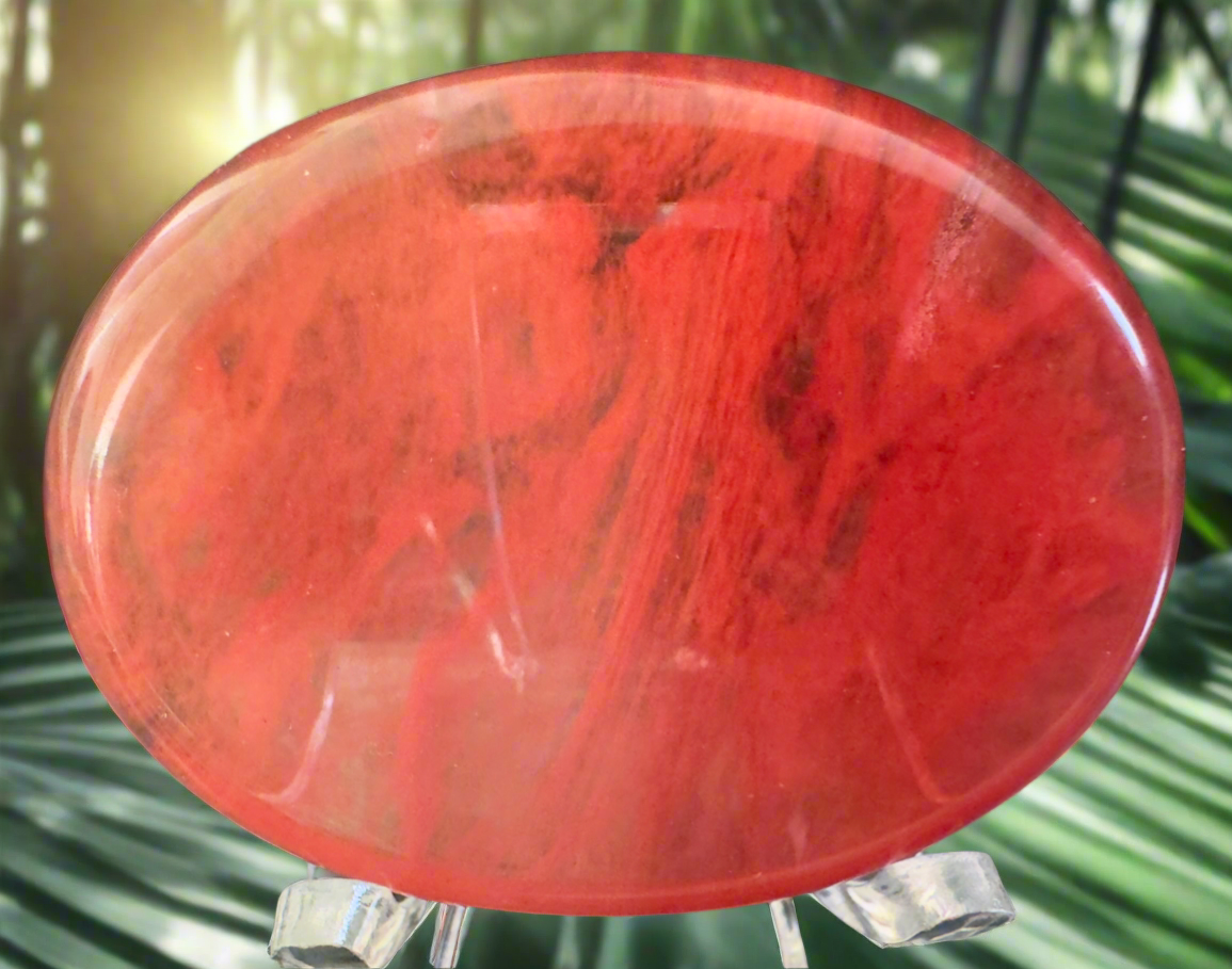Close-up of a polished, red stone disc on a clear plastic stand.