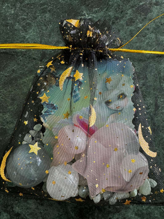 A black mesh bag with gold stars and moon designs filled with crystals sits on a green marble surface.