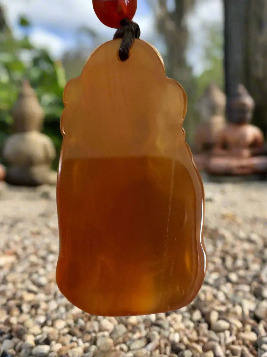 Amber pendant with brown cord against a backdrop of pebbles and Buddha statues.