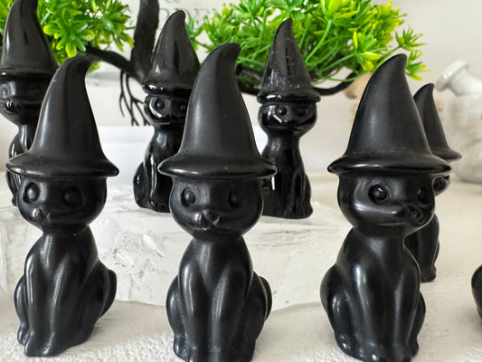 Several black obsidian cat figurines wearing witch hats on a white surface.