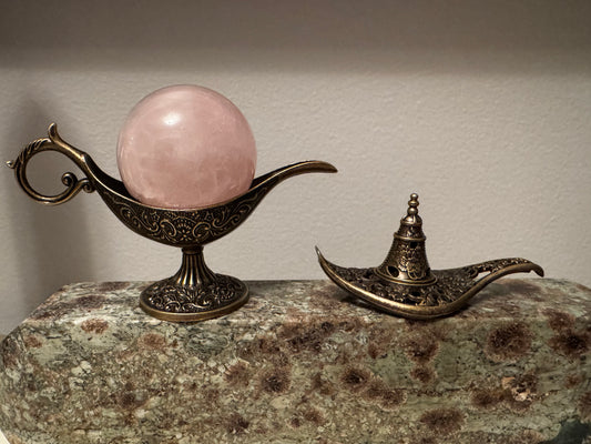 Rose quartz crystal in ornate genie lamp on decorative stone.