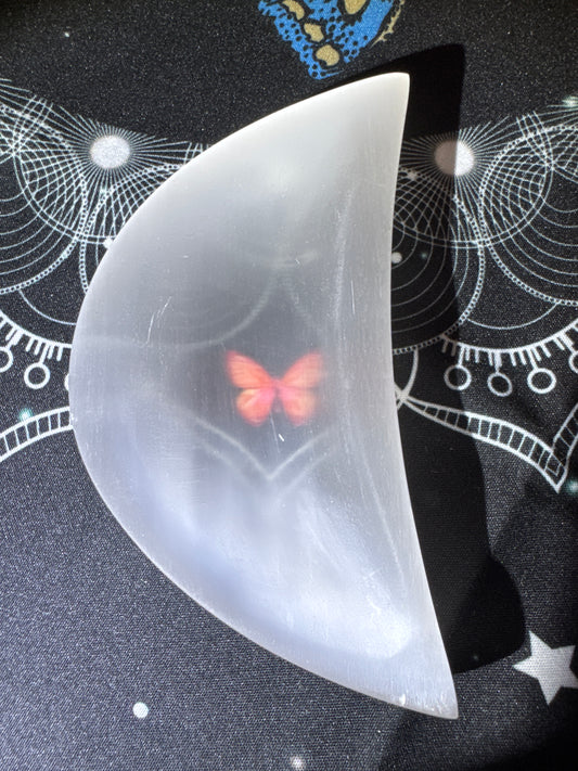White selenite moon with embedded butterfly on patterned cloth.