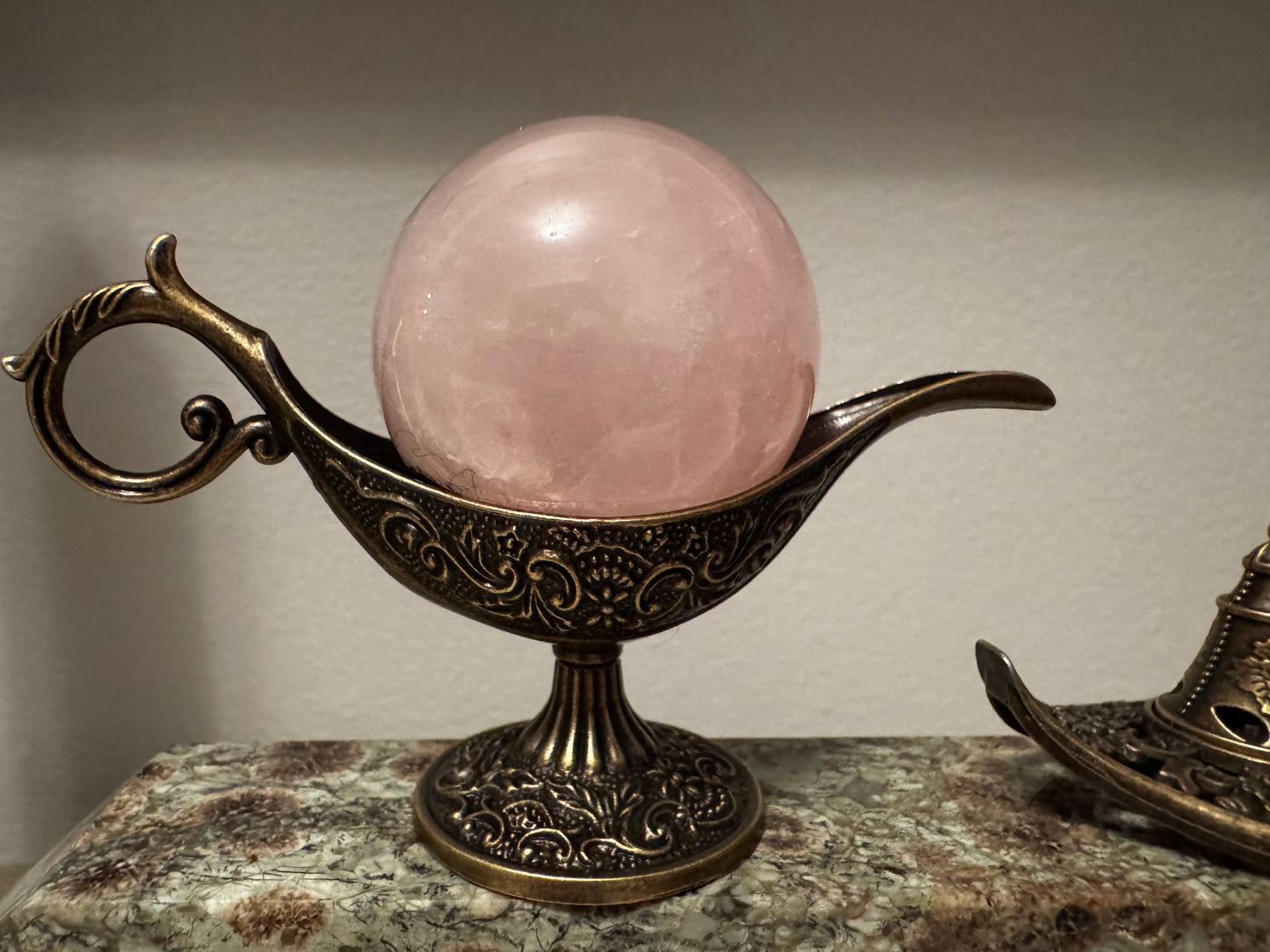A rose quartz sphere in a decorative, bronze-colored lamp.