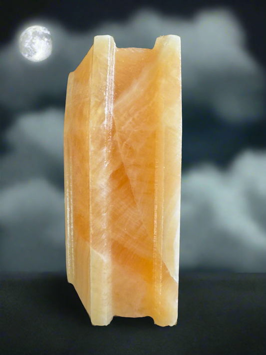 An orange and white calcite stone statue in front of a cloudy night sky with a full moon.