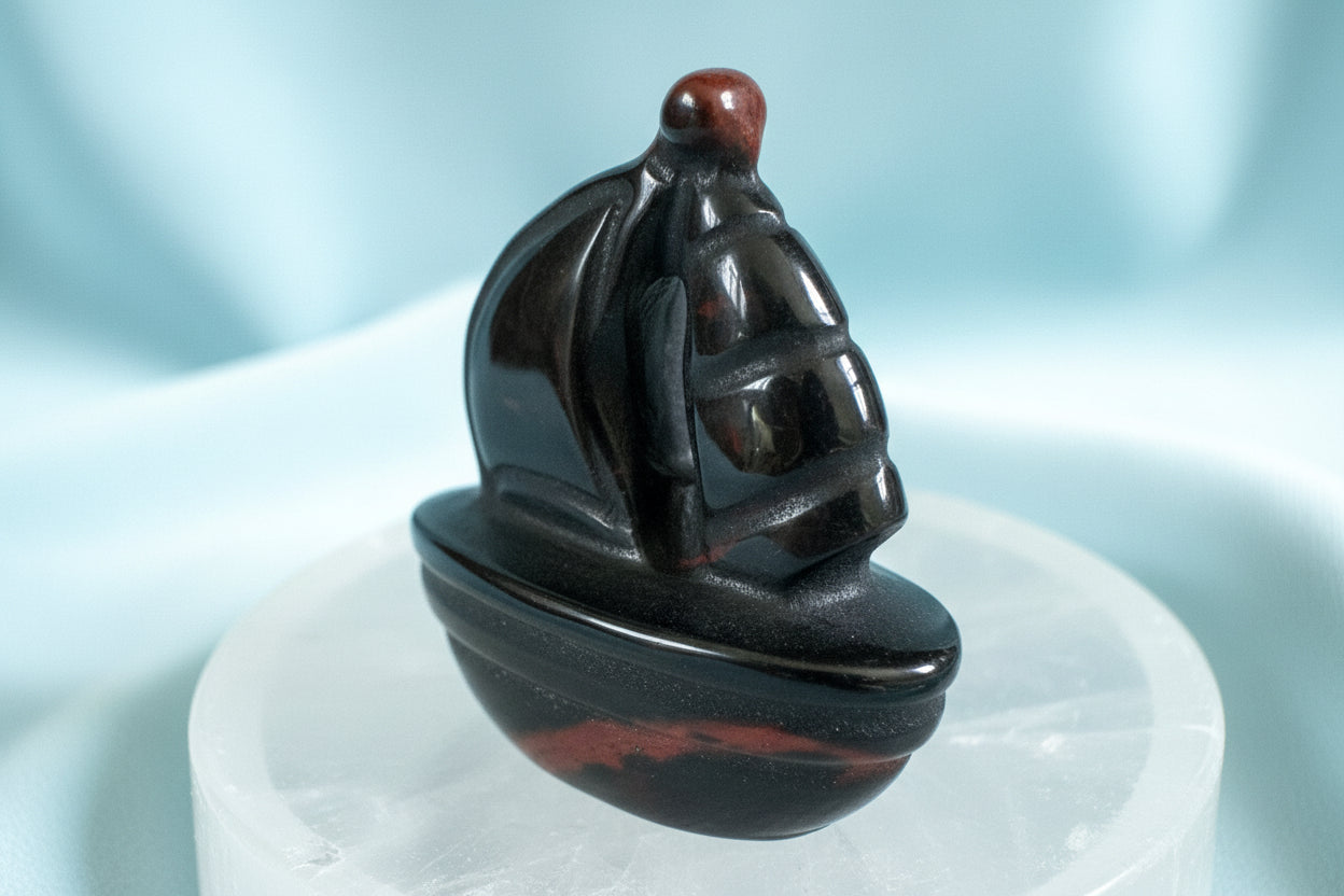 obsidian carving of a sailboat on a clear quartz stand