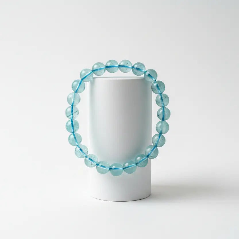 close up looking down at a 9mm aquamarine bead bracelet with blue thread and an off white background