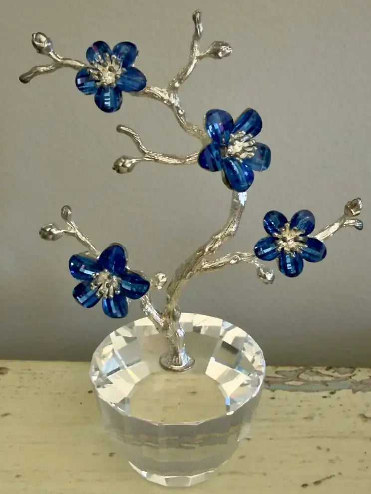 A decorative crystal tree with silver-toned branches, four blue faceted flower blossoms, and a clear faceted glass base, shown against a neutral background.