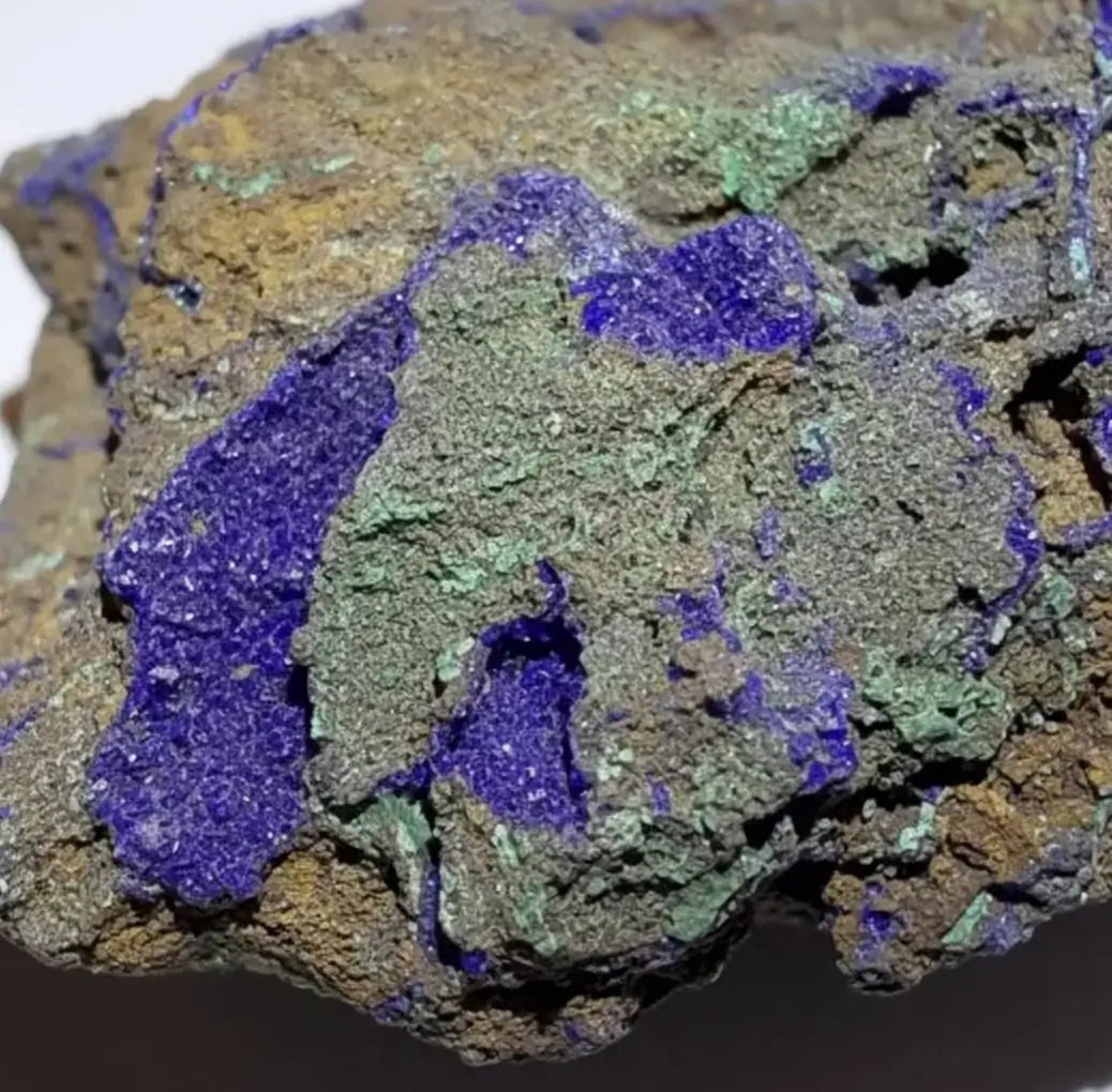 A close-up of a mineral specimen showing vivid purple-blue lapis lazuli-like crystals over a brown and green matrix.
