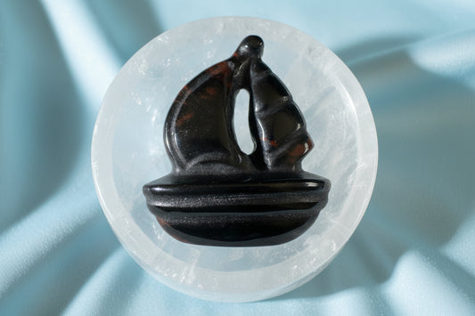 Carved obsidian sailboat on a selenite bowl.