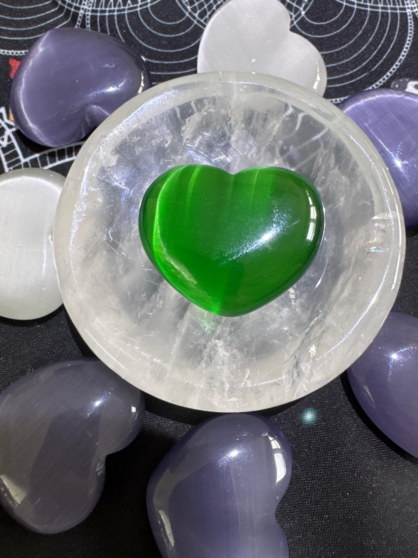 Overhead shot of green and purple heart-shaped crystals arranged around a clear quartz bowl containing a green heart-shaped crystal.