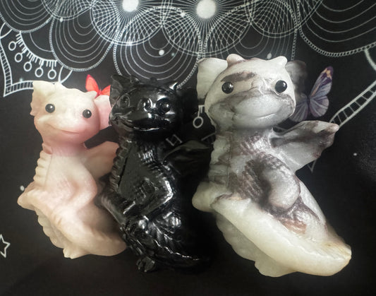 Three dragon figurines, pink, black, and marble, on a patterned black background.