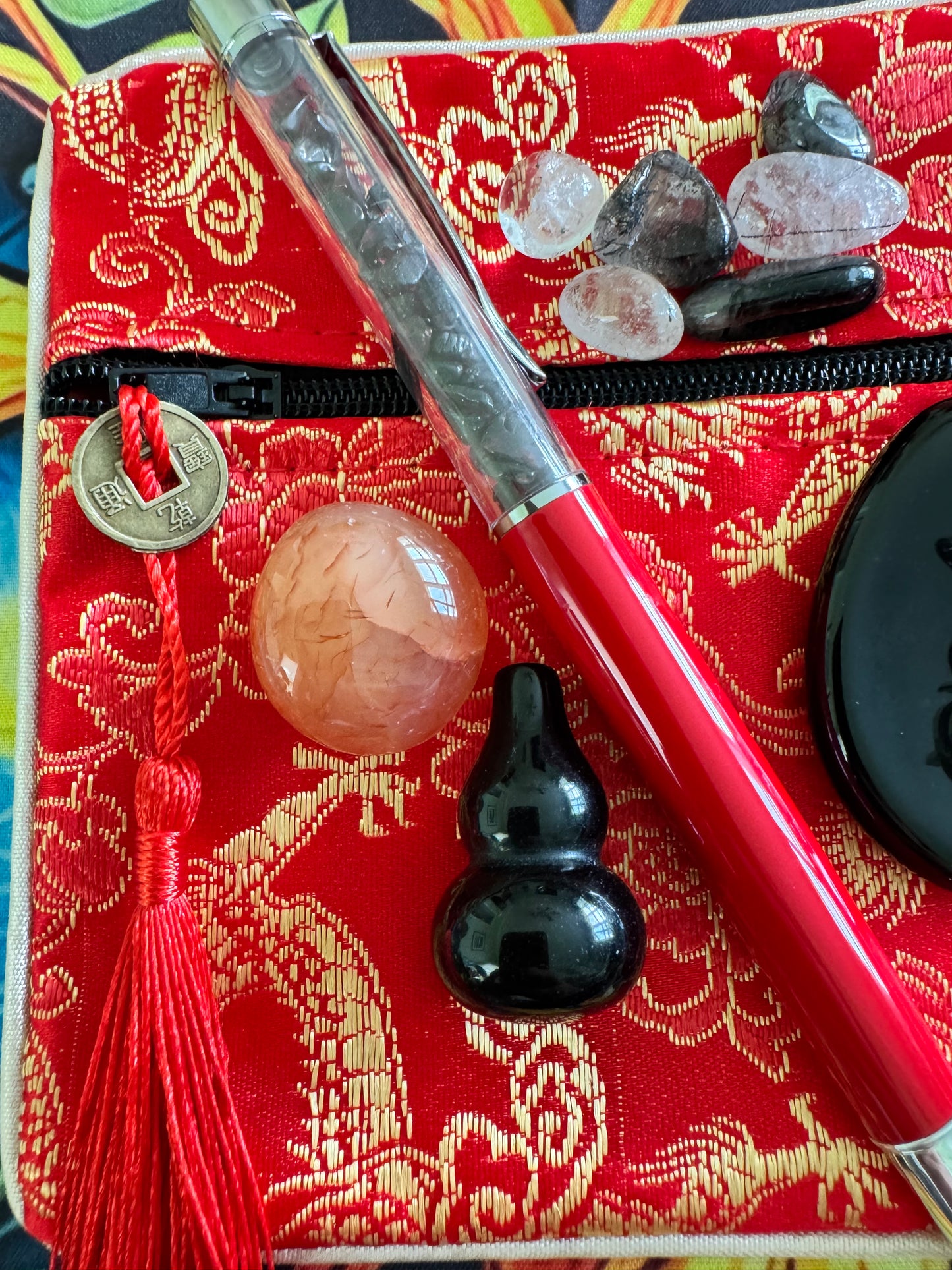 Red fabric pouch with gold pattern, red tassel, pen, crystals, and black gourd.