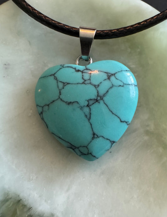 Close-up of a turquoise heart pendant with black veins hanging from a black cord.