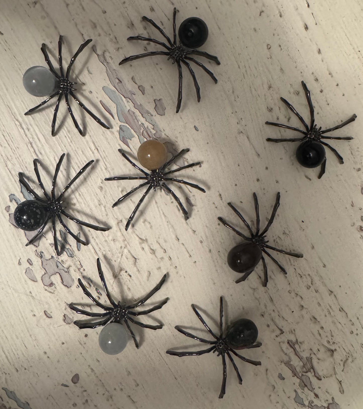 Eight decorative spiders with bead bodies on a weathered white surface.