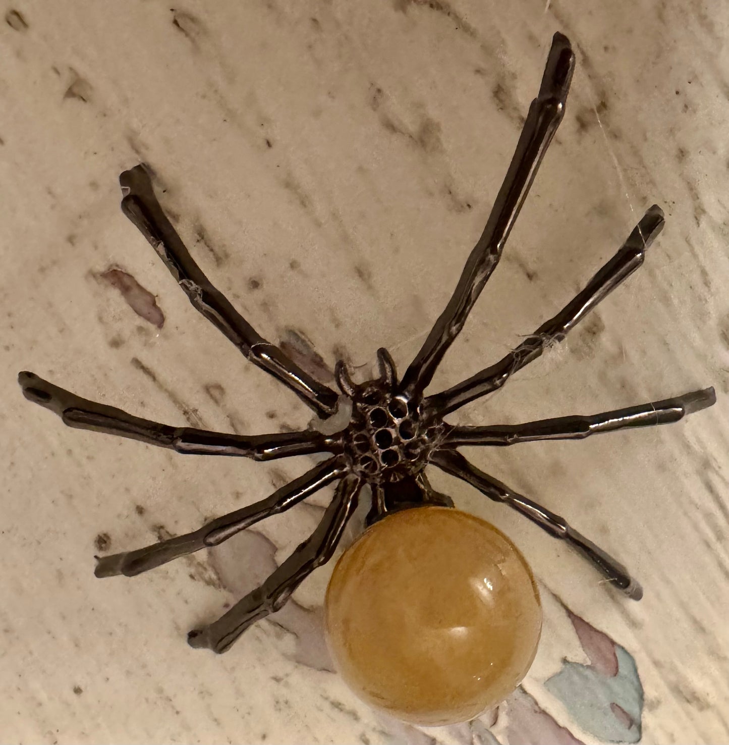 Brooch in the shape of a black spider with an amber-colored round body on a marble surface.
