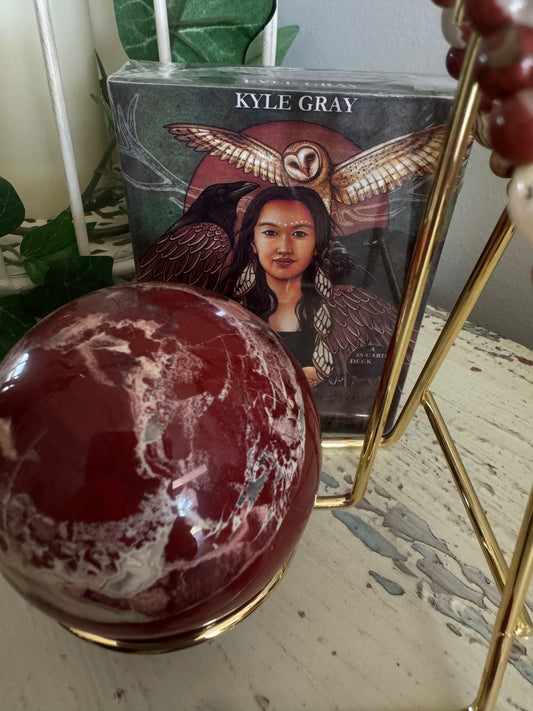 A red and white crystal ball sits next to a Kyle Gray tarot deck on a white surface with blue-grey designs.