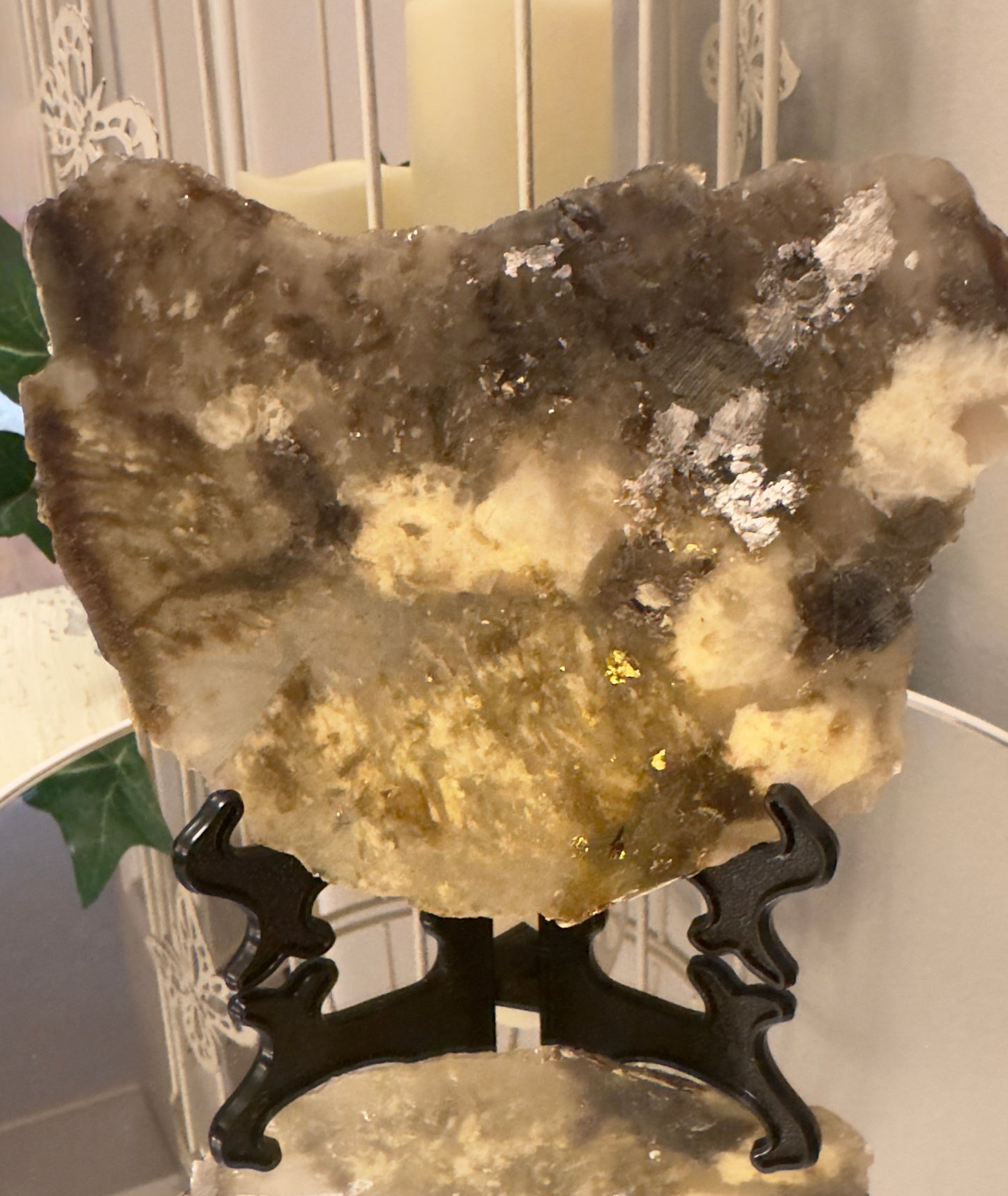 Stone art piece with gold and silver embellishments on a black display stand.