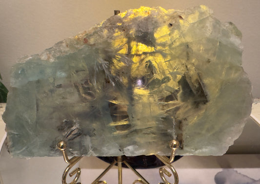 Backlit chunk of blue-green fluorite on a gold stand.