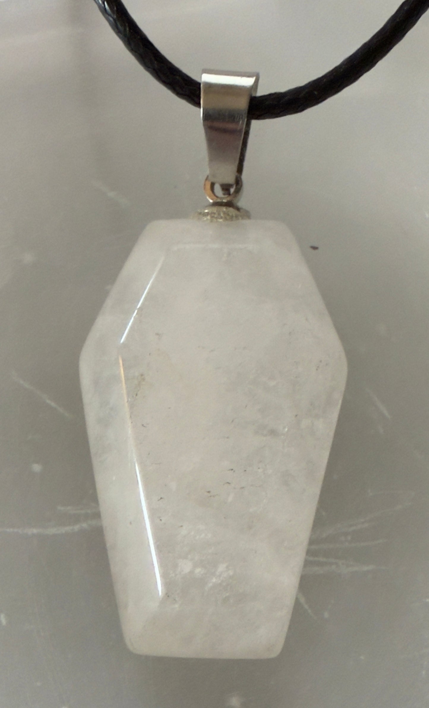 A white coffin-shaped quartz crystal pendant with a silver bail hanging on a black braided cord.