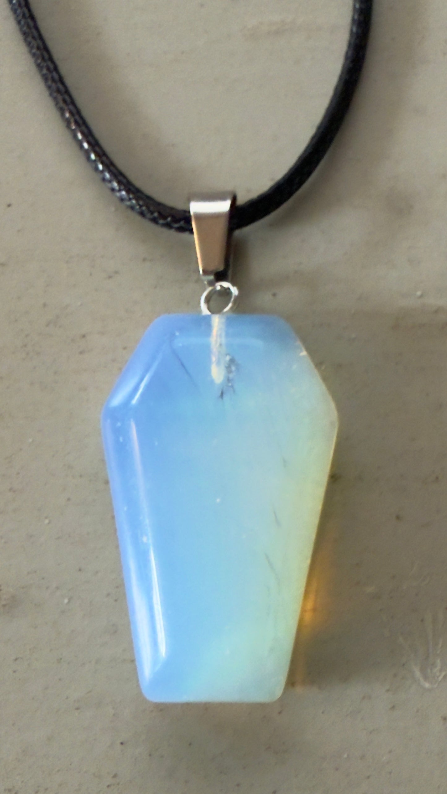 Close-up of a blue and yellow coffin-shaped opal pendant on a black cord.