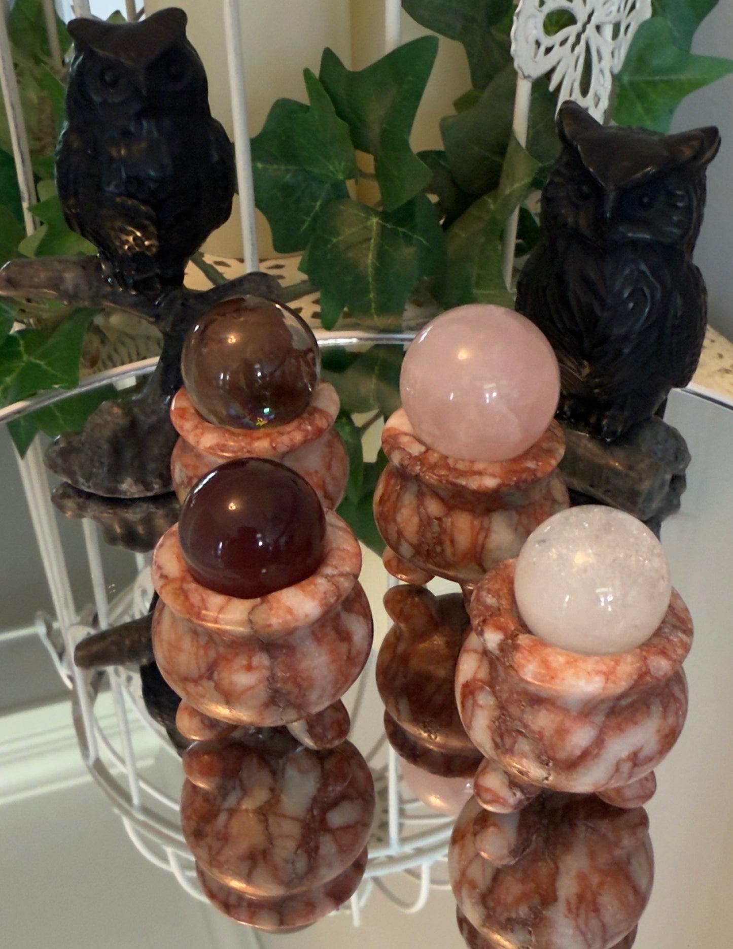 Four crystal spheres in marble holders with two owl figurines on a mirrored surface.