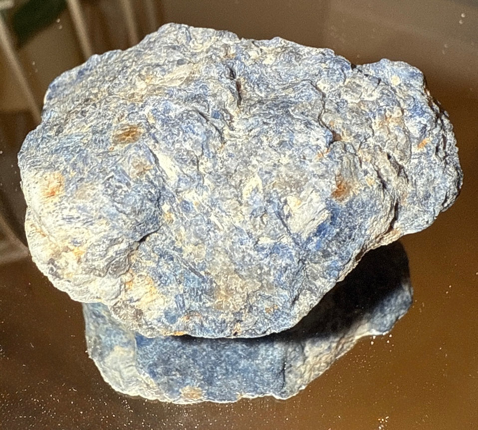 A rough, blue and white stone sits atop a reflective surface.
