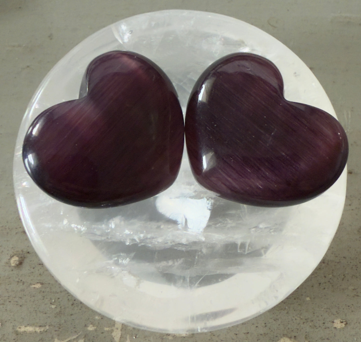 Two purple heart-shaped polished stones on a white selenite plate.