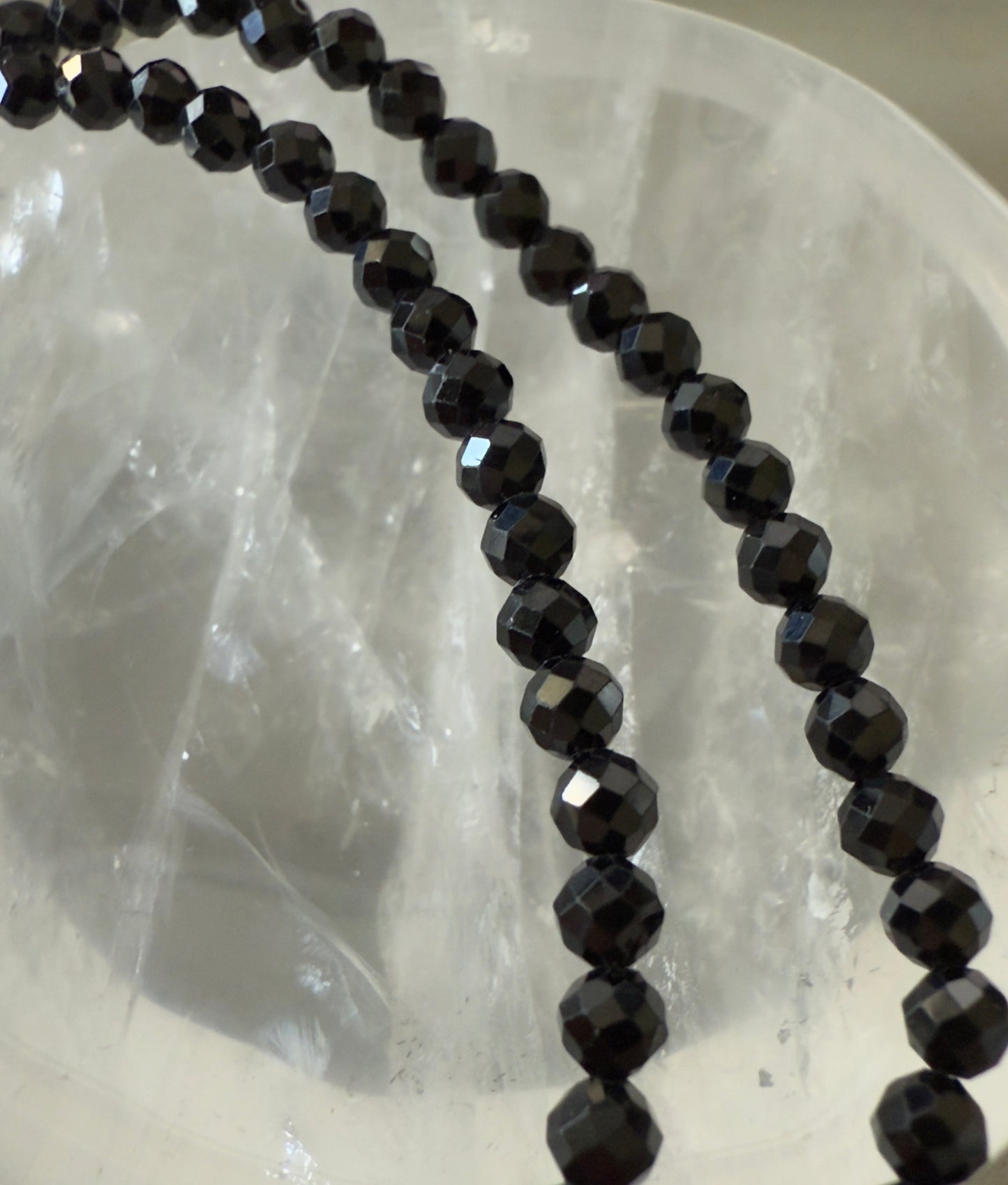 Two strands of faceted black beads lie against a translucent crystal bowl.