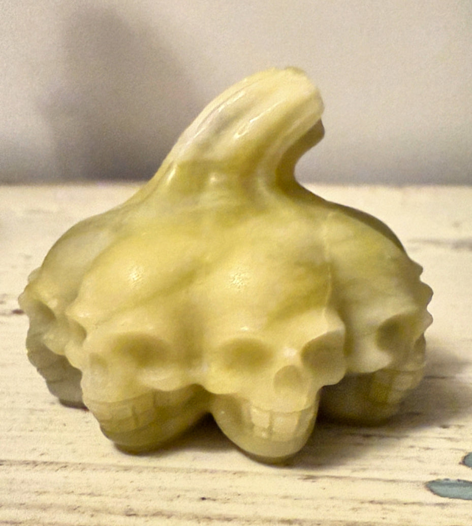 A translucent, yellowish carving of skulls arranged in a cluster with a long, smooth protrusion rising from the top.