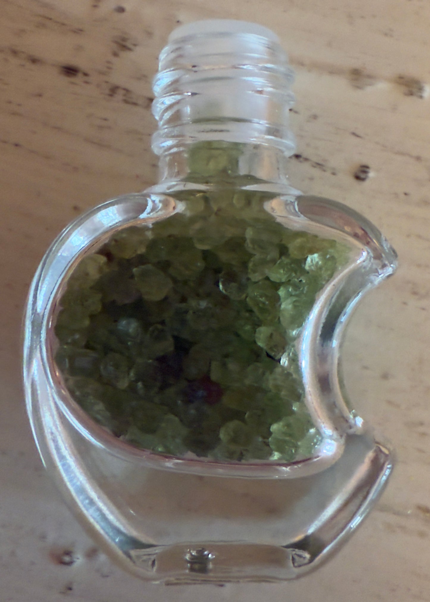 Clear, apple-shaped bottle filled with green stones.