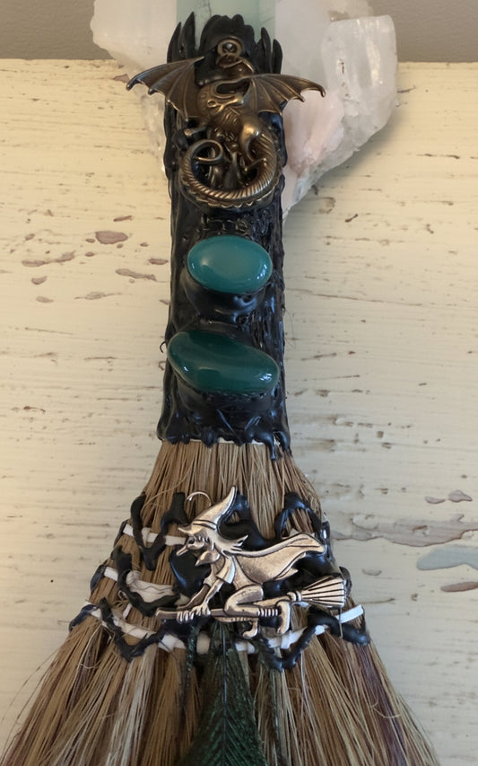 Close-up of a decorative witch's broom with dragons, stones, and a witch figure.