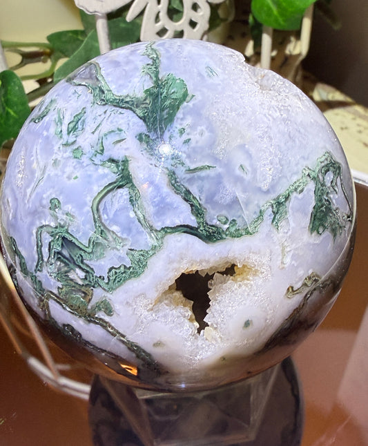 close up of green and white tree agate crystal sphere on a small stand pocket is filled with clear quartz crystals