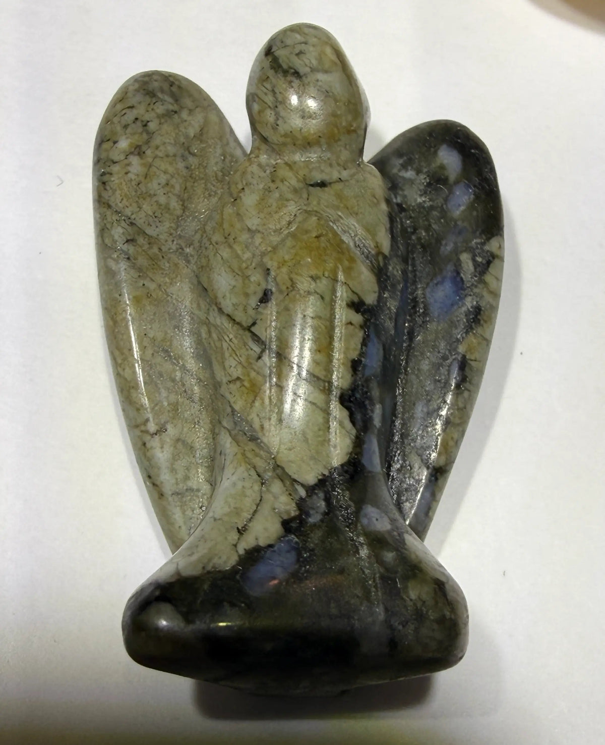 Photo of larvikite hand carved angel, Blue schiller from feldspar causing flash visible. carving resting on a white background