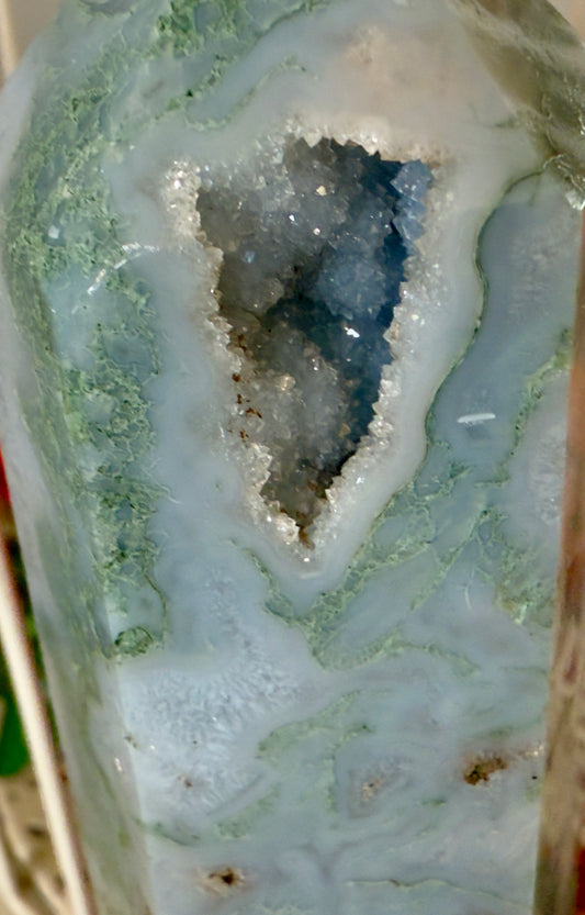 Natural Dark Green Moss Agate Tower with Druzy Pockets in front of a bird cage with autumn flowers behind