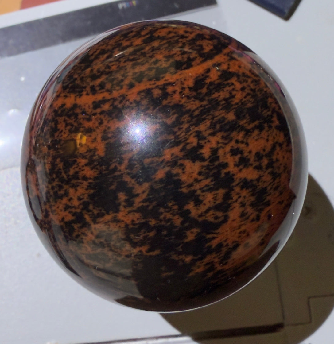 Polished mahogany obsidian sphere with deep chocolate brown and black patterns, natural gemstone crystal ball for metaphysical decor, grounding, and crystal healing from Mainstreet Crystals and Minerals.