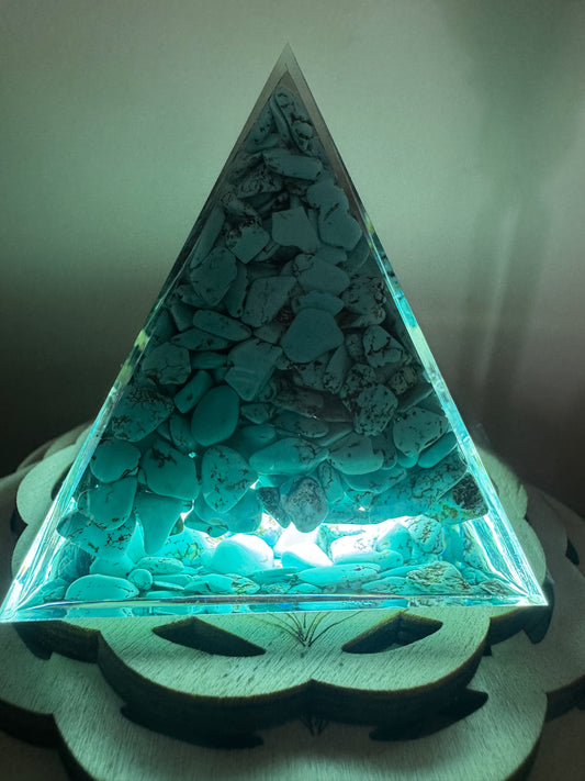 A turquoise stone pyramid on a carved wooden base, illuminated with a light.