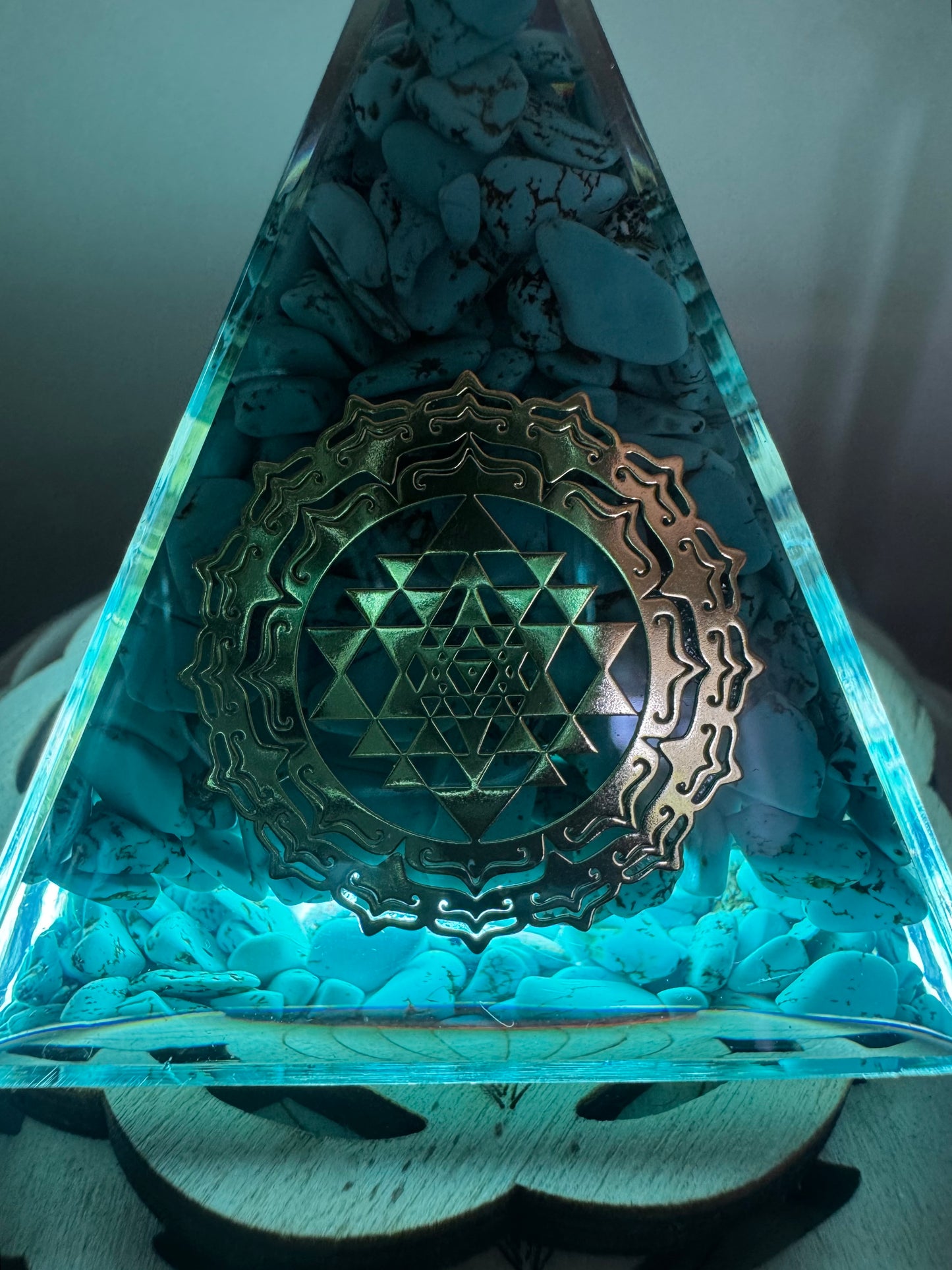 Illuminated turquoise pyramid with stones and golden geometric emblem.