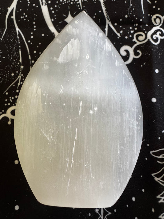 A white selenite crystal on a black and white patterned surface.