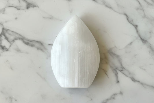 A white selenite crystal on a black and white patterned surface.
