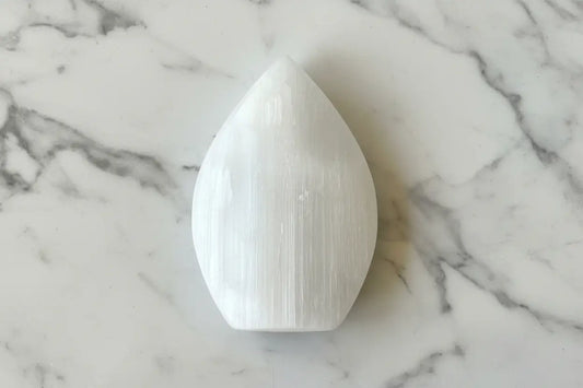 A white selenite crystal on a black and white patterned surface.