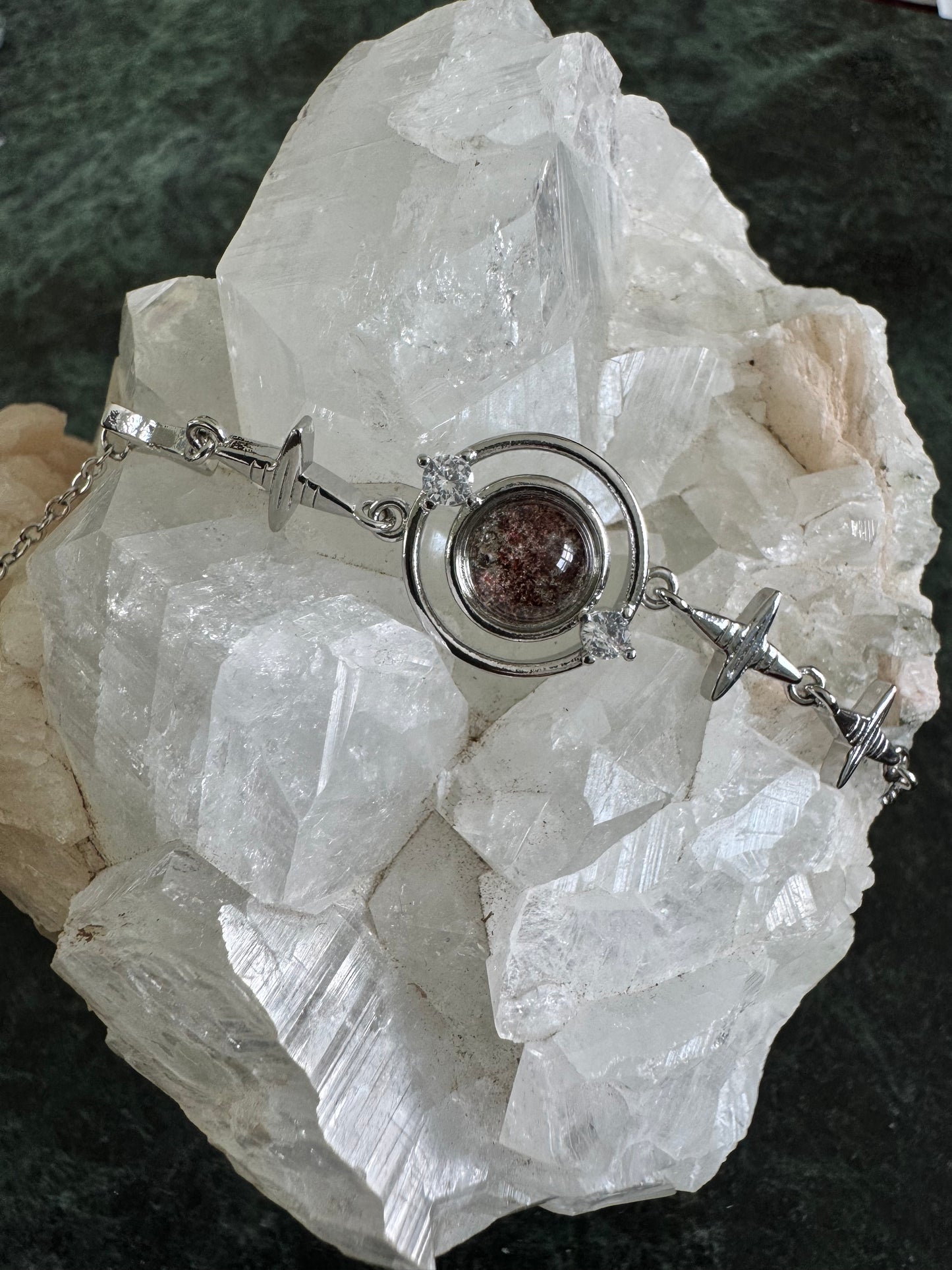 Silver bracelet with red stone and diamond accents, displayed on a white crystal.