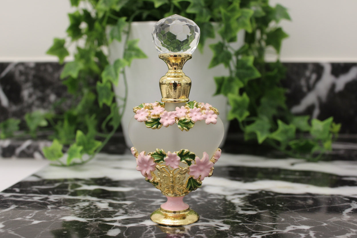 pink and green flowers on a gold tone mini frangrance bottle on a counter with ivy behind