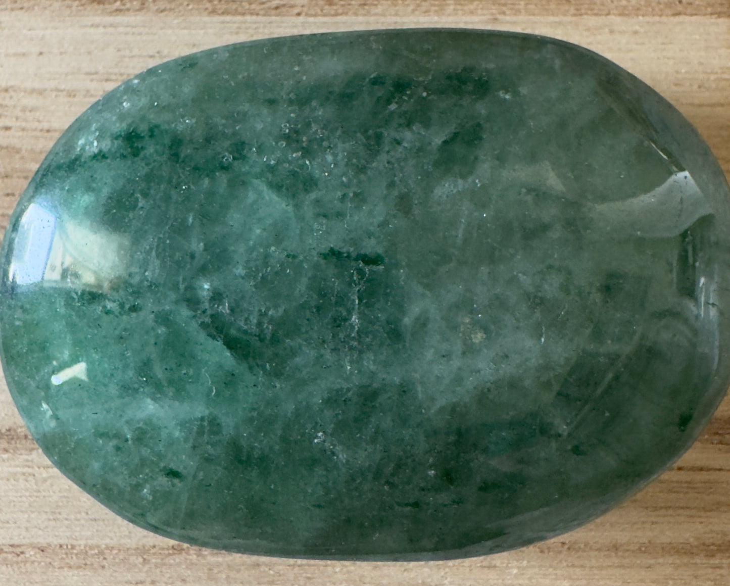 Polished green crystal stone on wood surface.