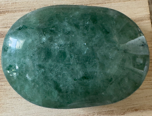 Polished green aventurine palm stone on wood.